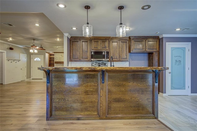 kitchen with baseboards, ornamental molding, stainless steel microwave, and visible vents