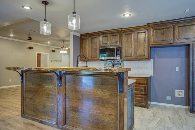 kitchen featuring pendant lighting, baseboards, stainless steel microwave, a ceiling fan, and backsplash