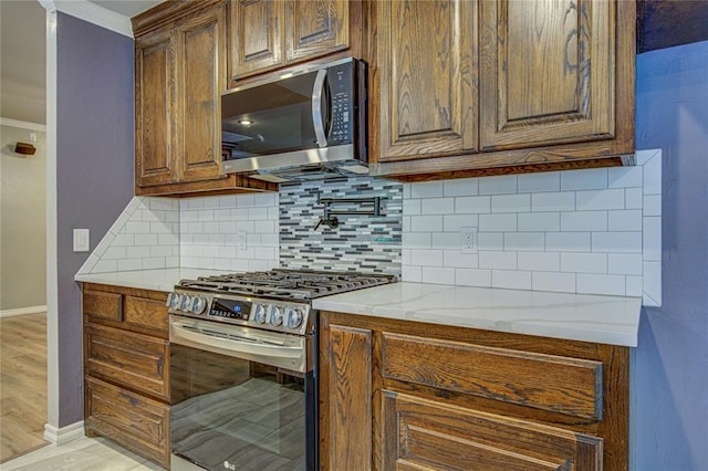 kitchen with backsplash, crown molding, appliances with stainless steel finishes, light wood-type flooring, and baseboards