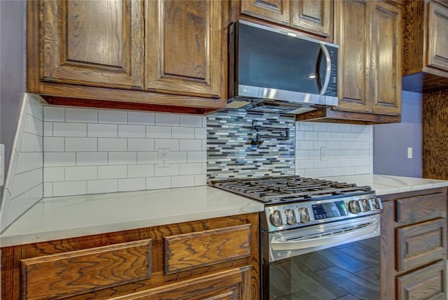 kitchen with stainless steel appliances, light stone counters, brown cabinetry, and tasteful backsplash