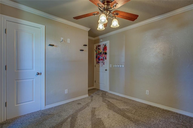 carpeted spare room featuring crown molding, baseboards, and a ceiling fan