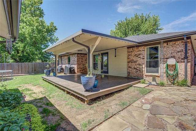 rear view of house featuring fence, a wooden deck, a yard, and brick siding