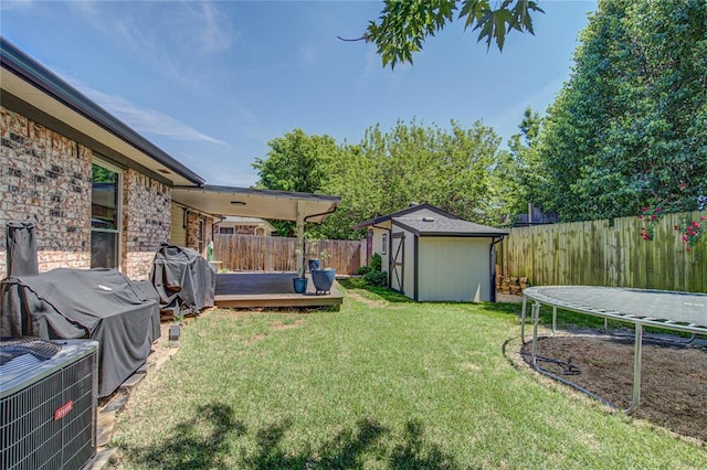 view of yard featuring a trampoline, a shed, a deck, a fenced backyard, and an outdoor structure