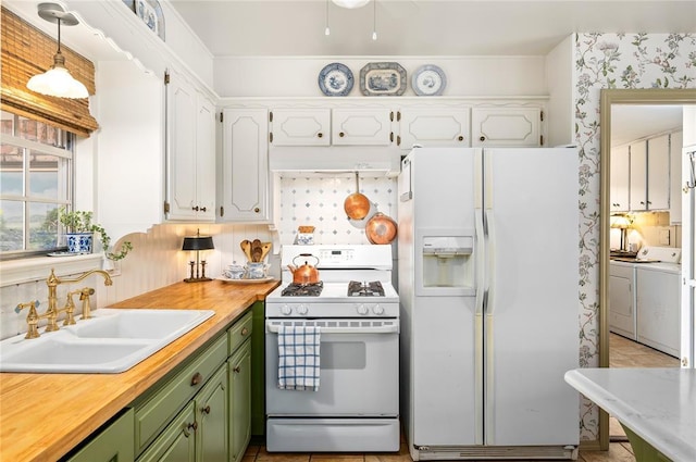 kitchen with washing machine and dryer, white appliances, under cabinet range hood, a sink, and green cabinets
