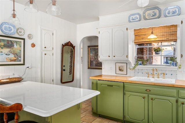 kitchen featuring light tile patterned flooring, a sink, arched walkways, backsplash, and dishwashing machine