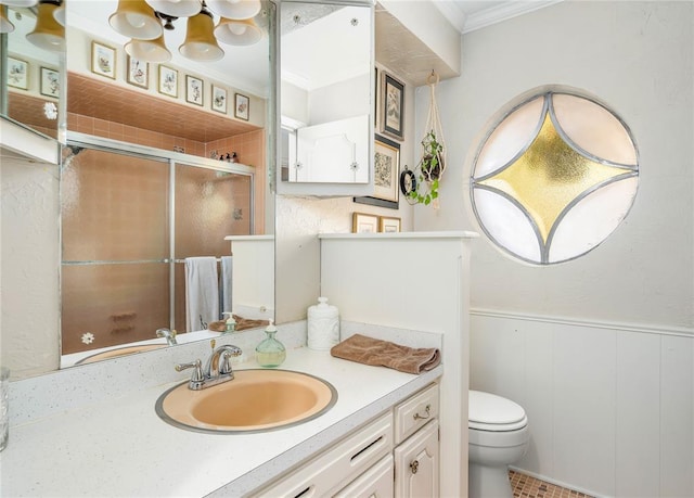 bathroom with crown molding, vanity, toilet, a wainscoted wall, and a stall shower