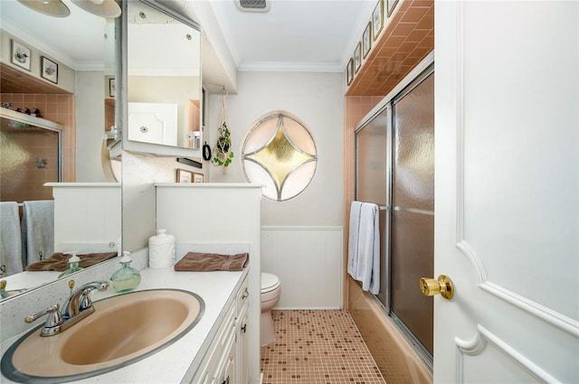 full bath featuring crown molding, vanity, toilet, a wainscoted wall, and combined bath / shower with glass door