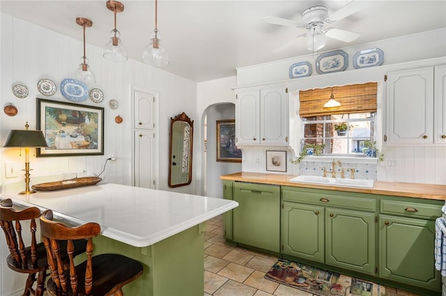 kitchen featuring dishwashing machine, a breakfast bar area, arched walkways, white cabinets, and a sink