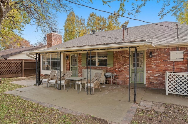 rear view of house featuring a chimney, roof with shingles, a patio area, brick siding, and fence