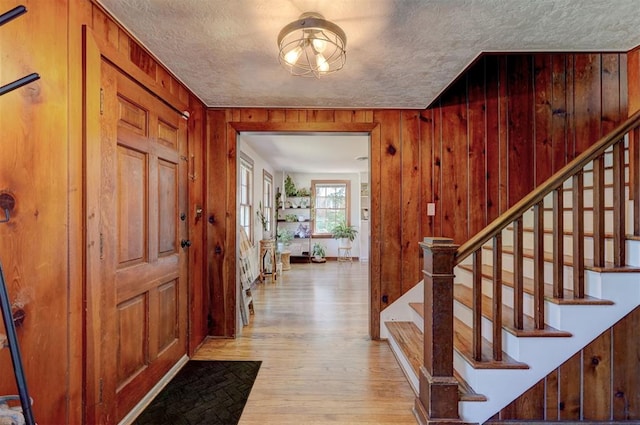 entryway featuring wood-type flooring, wood walls, a textured ceiling, and stairs