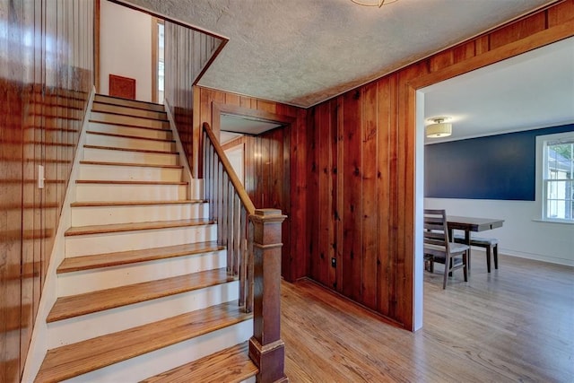 staircase with wooden walls, baseboards, a textured ceiling, and wood finished floors