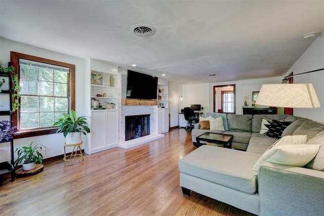 living area with visible vents, built in features, a fireplace, light wood-type flooring, and baseboards