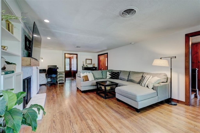 living room with a tiled fireplace, light wood finished floors, baseboards, and visible vents
