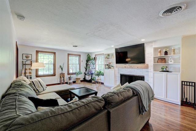 living area with a fireplace, a textured ceiling, built in shelves, wood finished floors, and visible vents