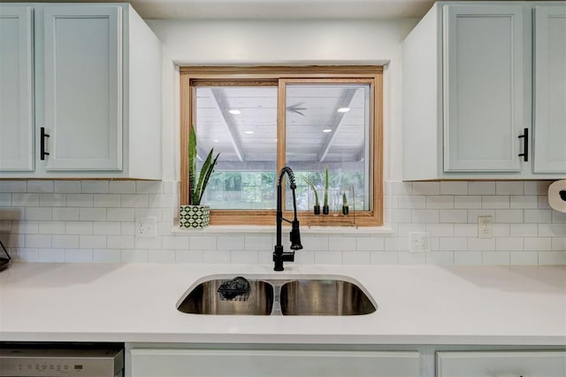 kitchen featuring light countertops, decorative backsplash, a sink, and dishwashing machine