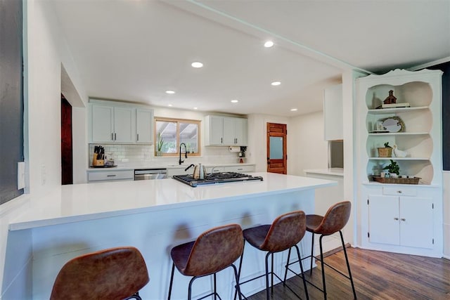 kitchen featuring gas cooktop, a kitchen breakfast bar, backsplash, dark wood-style flooring, and a sink