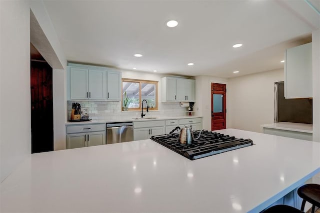 kitchen featuring a sink, dishwasher, a breakfast bar area, light countertops, and tasteful backsplash