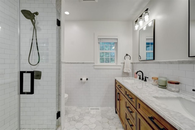 bathroom with tile walls, wainscoting, a shower stall, a sink, and tile patterned floors