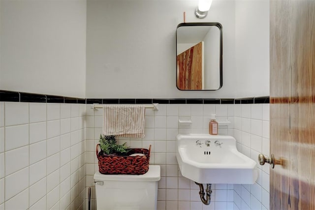 bathroom featuring toilet, tile walls, wainscoting, and a sink
