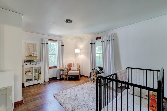 bedroom with visible vents, wood finished floors, a nursery area, and multiple windows