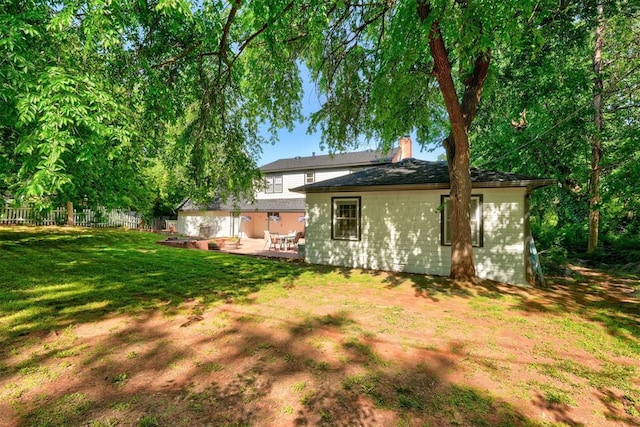 back of property featuring fence, a yard, and a chimney