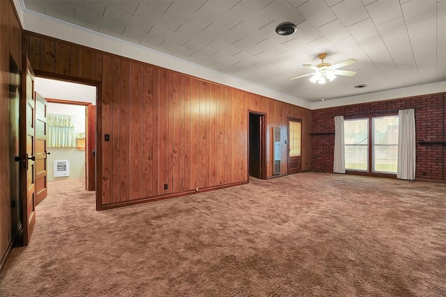 interior space with ceiling fan, visible vents, carpet floors, wooden walls, and heating unit