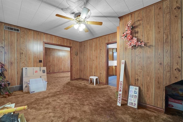 interior space featuring carpet flooring, a ceiling fan, wood walls, and visible vents