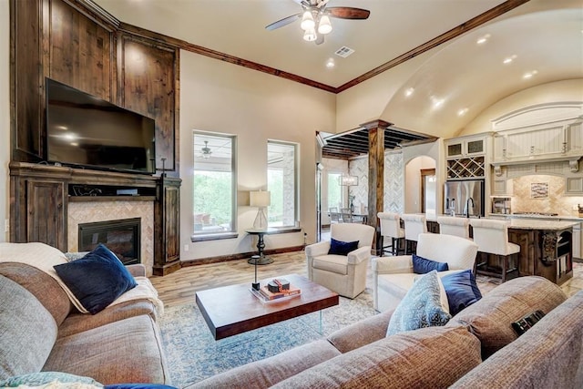 living room featuring ceiling fan, light wood-style floors, a glass covered fireplace, baseboards, and lofted ceiling