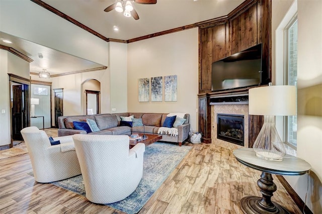 living room featuring ceiling fan, a fireplace, arched walkways, wood finished floors, and ornamental molding