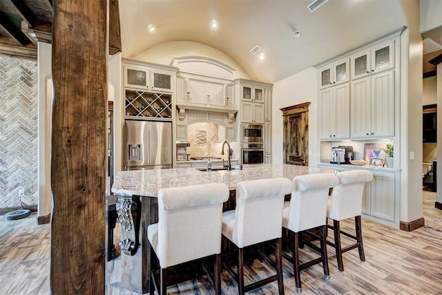 kitchen with light stone counters, appliances with stainless steel finishes, a sink, a kitchen island with sink, and a kitchen bar