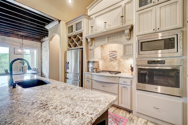 kitchen featuring appliances with stainless steel finishes, tasteful backsplash, arched walkways, a sink, and glass insert cabinets