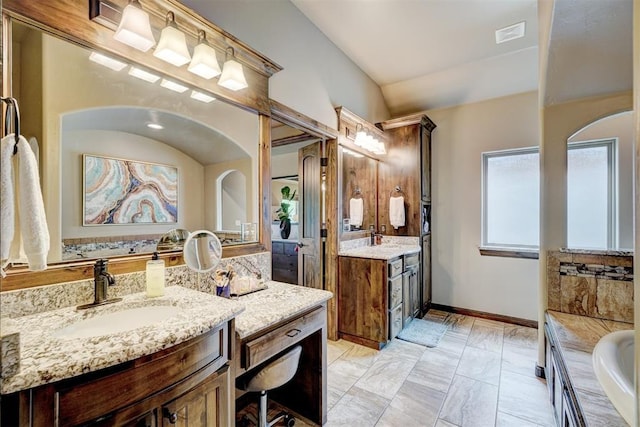 full bath featuring a sink, vaulted ceiling, a bathtub, and two vanities