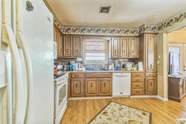 kitchen with a sink, light wood finished floors, white appliances, backsplash, and visible vents