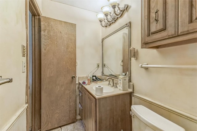 bathroom featuring vanity, toilet, and a wainscoted wall