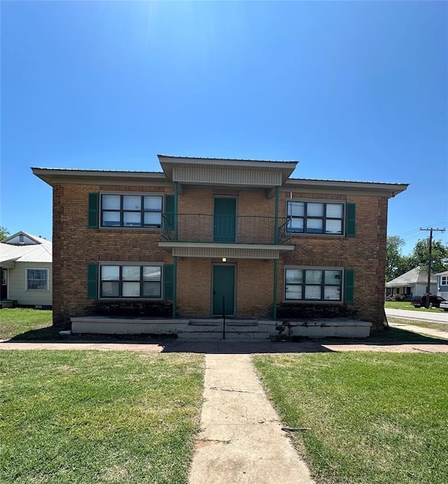 view of front of property featuring a front lawn, brick siding, and a balcony