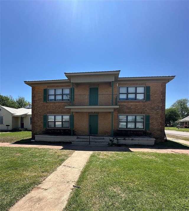 view of front facade featuring brick siding, a balcony, and a front lawn