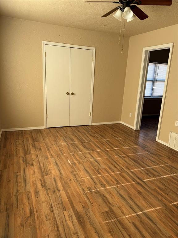unfurnished room with a textured ceiling, ceiling fan, visible vents, and wood finished floors