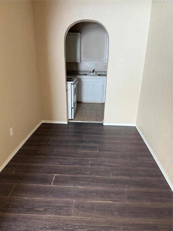 unfurnished room with arched walkways, baseboards, dark wood finished floors, and a sink