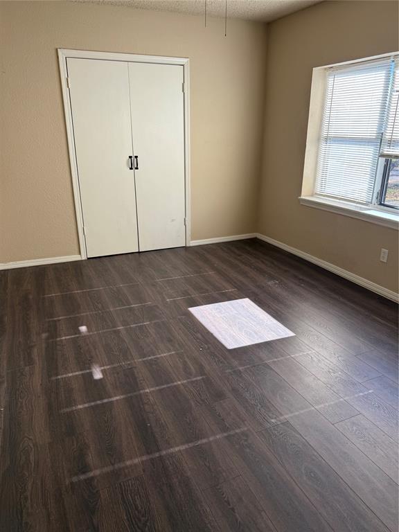 unfurnished bedroom featuring baseboards, dark wood-style floors, and a closet