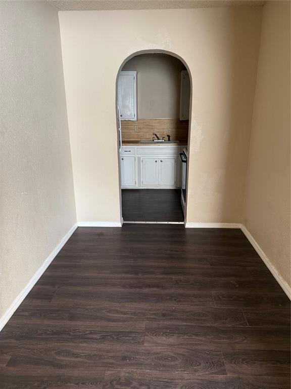 unfurnished room with a sink, arched walkways, baseboards, and dark wood-style flooring