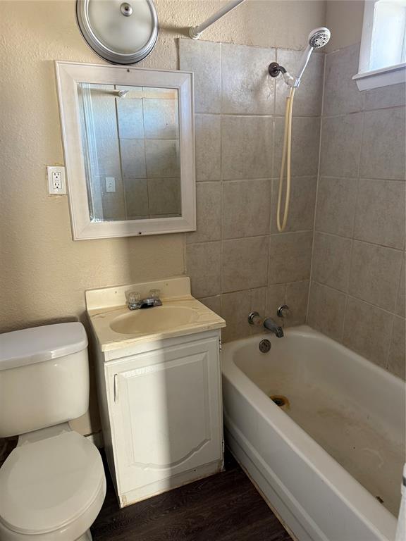 full bath with shower / bathing tub combination, wood finished floors, vanity, toilet, and a textured wall
