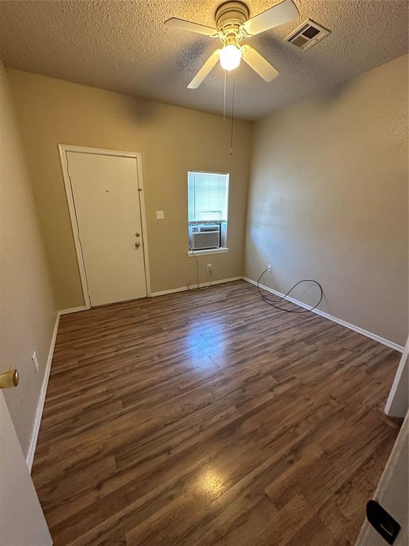 spare room featuring a textured ceiling, ceiling fan, visible vents, and wood finished floors