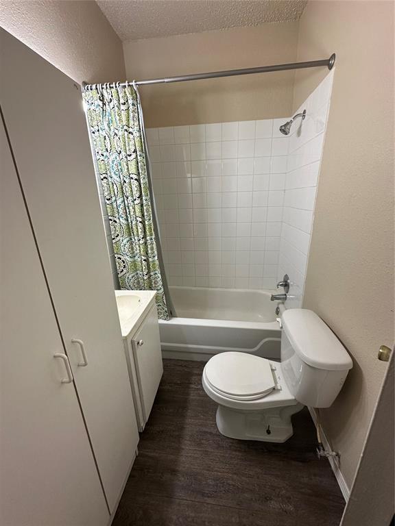 full bathroom with vanity, shower / bath combo with shower curtain, toilet, a textured ceiling, and wood finished floors