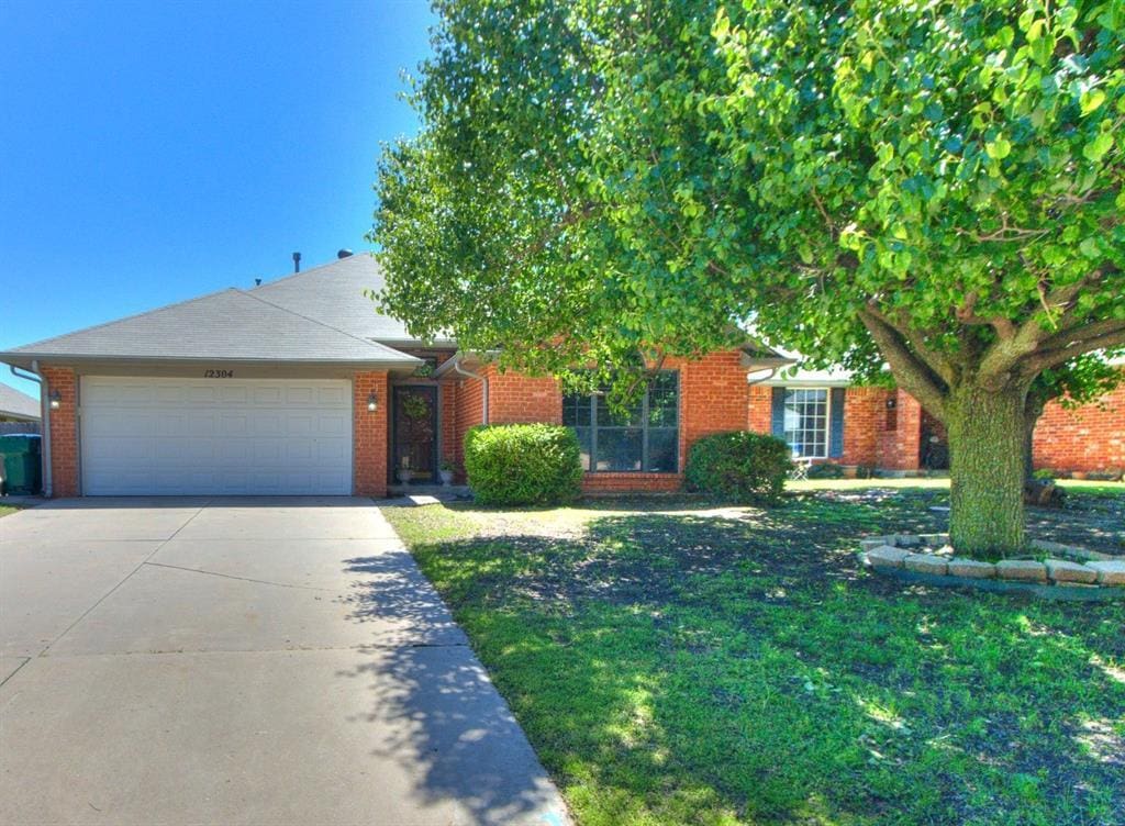 12304 SW 11th St, Yukon, OK 73099 - view of front of property with an attached garage, concrete driveway, a front lawn, and brick siding