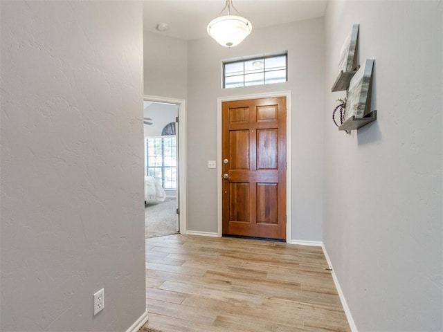 foyer featuring light wood-style floors, baseboards, and a textured wall