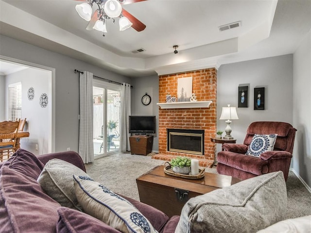 carpeted living room with visible vents, a raised ceiling, ceiling fan, and a fireplace