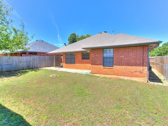 back of property featuring a fenced backyard, a lawn, roof with shingles, and brick siding