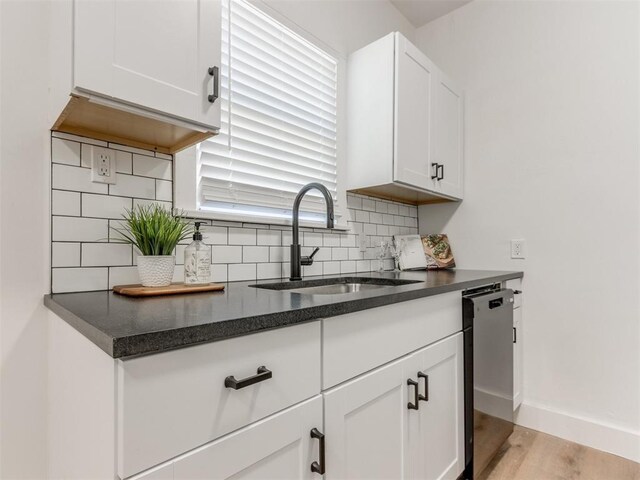 1132 NE 17th St, Oklahoma City, OK 73111 - kitchen featuring a sink, light wood-style flooring, white cabinetry, decorative backsplash, and stainless steel dishwasher