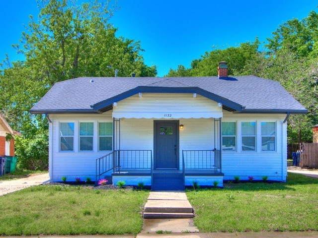 1132 NE 17th St, Oklahoma City, OK 73111 - bungalow featuring a front lawn, roof with shingles, covered porch, and a chimney