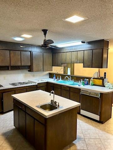 kitchen featuring a textured ceiling, dishwasher, a sink, light countertops, and white gas cooktop